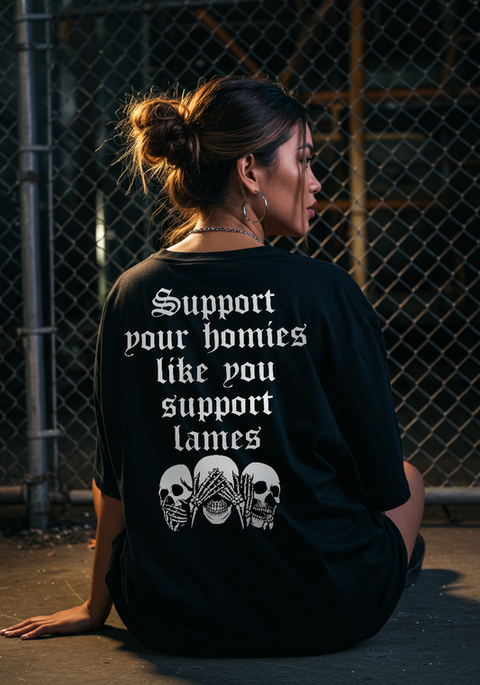 Person wearing a black t-shirt with text and graphic designs, sitting against a chain-link fence. Support your homies T-Shirt 